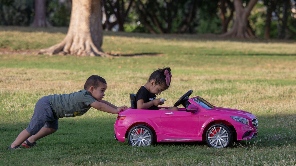 Zwei Kinder spielen mit einem pinken Elektro-Kinderauto im Park